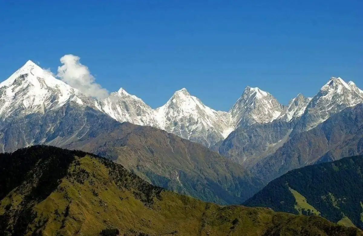 “A panoramic view of Darma Valley with traditional Himalayan villages in the foreground and the snow-covered Panchachuli peaks towering in the background under a clear blue sky.”